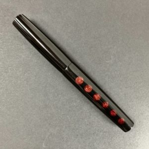 Closed pen showing shiny black material with a row of coppery garnet coloured circles of diminishing diameter
