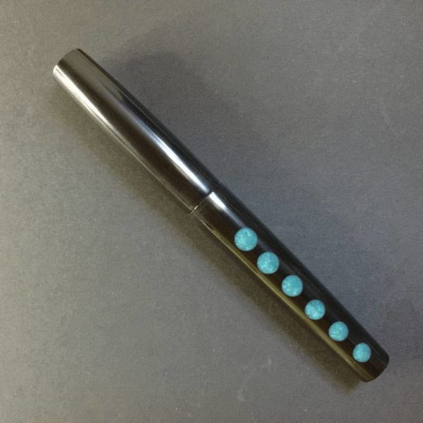 Showing a black fountain pen with a row of turquoise 'moons' along the barrel