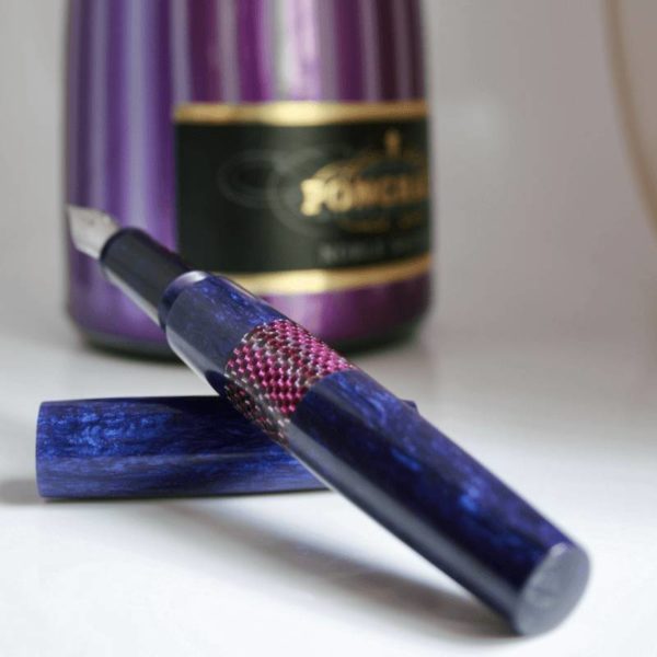 Perlé Pen against a backdrop of a bottle of sparkling wine label in stripes of violet and white