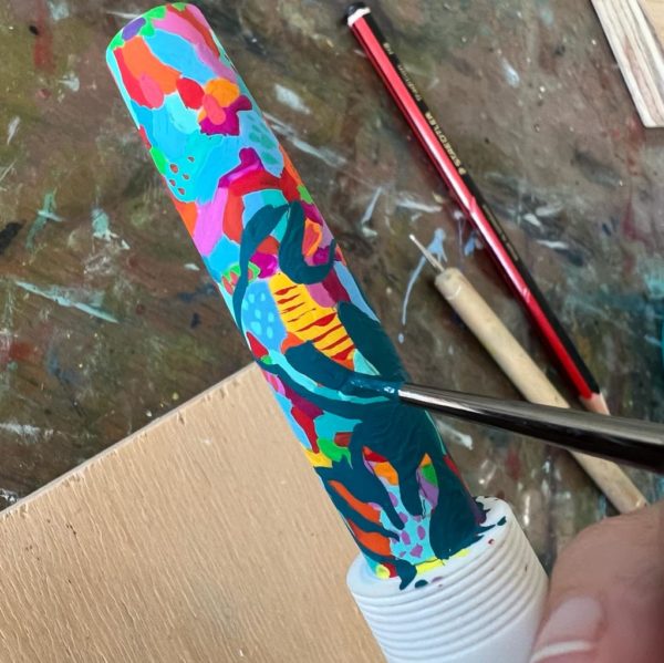 Painting a solid turquoise around the outside of a shape around the outside of a fish shape, leaving behind brightly coloured left-over paint